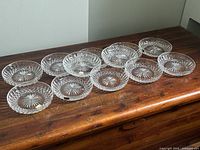 12 clear English crystal dessert bowls arranged on a wooden surface, showing intricate cut starburst and diamond pattern designs.