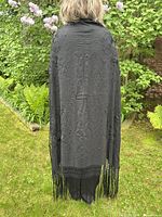 View of shawl worn on back showing floral embroidery detail in black silk and fringe at bottom edge