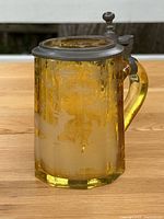 Front view of amber-stained glass beer stein with pewter lid showing etched hunting scene
