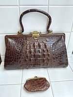 Front view of brown crocodile leather handbag with matching coin purse placed below it, both showing crocodile skin texture and brass hardware.