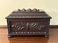 Front view of antique carved oak tea caddy box showing carved floral and leaf design and small feet.