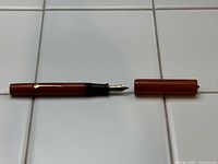 Photo of the uncapped reddish-brown antique fountain pen with the 14K gold nib exposed lying horizontally on a tiled surface.