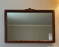 Front view of the rectangular mirror showing the wooden frame with a decorative oval medallion at the top center and clear mirror surface.