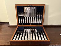 Full view of open wooden box containing 12 knives and 12 forks arranged in fitted slots