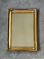 Full view of the small rectangular gilt wood framed mirror showing the ornate corner details and overall condition of frame and glass.