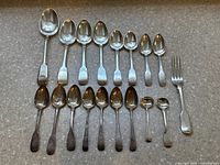 All silver spoons and one fork laid out on countertop showing full lot