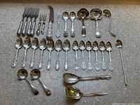 Full lot arranged showing forks top left, knives top right, serving spoons and ladles top row. Middle row displays tablespoons and teaspoons. Bottom row includes bouillon, shell spoons and ladles.