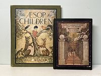 Two antique children's books standing upright side by side, the larger titled 'The Aesop for Children' with a color illustrated cover showing animals around a tree, and the smaller titled 'A Childs Garden of Verses' with an illustrated gate on the cover.