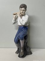 Front view of Bing & Grondahl porcelain figurine showing boy playing flute while sitting on a tree stump.