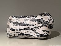 Side view of black and white zebra jasper stone sculpture showing striped pattern and rounded top profile.