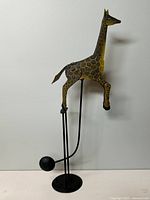 Full view of hand-painted metal giraffe balanced on one leg attached to a black metal base with weighted ball.