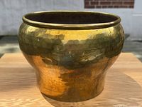 Front view of the large hand-hammered brass jardinière showing the full rounded shape and hammered texture, highlighting the reflective brass surface.