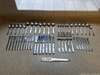 Full lot arranged on countertop showing all pieces including spoons, forks, knives, and letter opener.