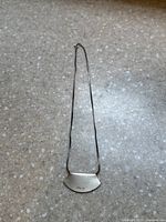 Full view of the sterling silver necklace with fan-shaped pendant on a speckled surface.