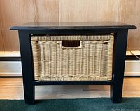 Frontal view of black wooden bench with wicker basket inserted, showing front and side parts of basket.