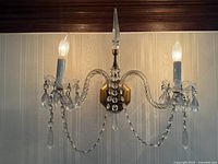Close-up of one brass and crystal wall sconce illuminated, showing detailed crystal drops and brass arms.