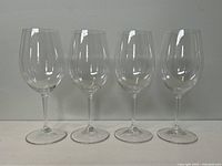 Set of four clear wine glasses arranged in a line, showing profile view and proportions.