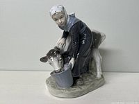 Front side view of Royal Copenhagen porcelain figurine showing girl feeding a calf with bucket.