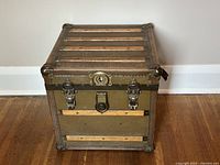 Front view of the small square antique trunk showing wood slats, metal corner protectors, and locking hardware.