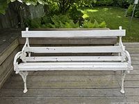 Front view of the white painted vintage garden bench showing cast iron arms and legs with decorative floral details and wooden seating slats with paint wear.