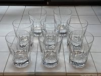 Eight heavy-bottomed crystal whisky glasses arranged in two rows on white tile surface.