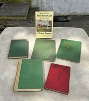 Overview of 6 vintage golf books on a table, covers visible in green and red cloth, one book with dust jacket standing upright.