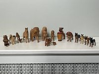 Wide shot of entire set showing 16 hand-carved wooden figurines on white shelf including dogs, deer and accordion player