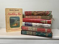 Single copy of Rainbow Classics edition of The Adventures of Huckleberry Finn standing beside stack of remaining six books