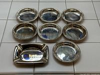 Overhead view of seven round coasters and one rectangular ashtray arranged on tiled surface.