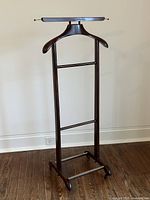 Full view of the vintage rolling wooden valet stand showing the curved top hanger, horizontal bars, and wheels at the base.