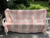 Full view of the wool throw blanket draped on an outdoor bench, showing its size and checkered pattern in pastel pink and cream colors.