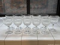 Photo showing 11 Webb Thomas Normandy pattern crystal wine goblets arranged in two rows on a white tiled surface by a window.