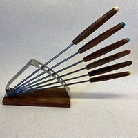 Full view of six teak-handled forks displayed in metal rack on teak base
