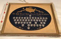 Frontal view of large rectangular framed display featuring 42 state quarters in capsules, some empty slots visible.