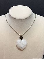 Photo of heart pendant with white Azeztulite and green Moldavite stones on silver chain displayed on necklace bust against black background