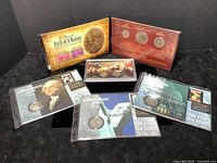 Overview of the full lot showing five items including three sets of coins in display sleeves and two stamp and coin collection folders.