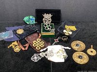 Overview of 17-piece lot of Celtic jewelry and amulets displayed on black fabric including brooches, pendants, rings, and amulets in pewter, silver, and gold-toned metals with stones and tartan ribbon.