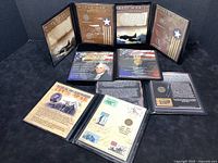 Several commemorative coin and stamp booklets displayed opened, showing historical details and coins inside.