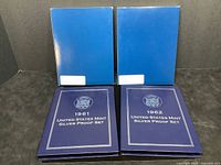 Two blue United States Mint Silver Proof Sets from 1961 and 1962 with original shipping sleeves visible.