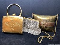 Front view of set of three vintage evening bags: gold painted wood bag with metal handle, rhinestone mesh bag with gold coil strap, brass and copper pillow-shaped bag with blue velvet interior.