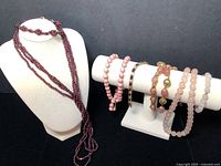 View of all jewelry pieces on display stands showing garnet multi-strand necklace, pink stone bead bracelets, and gold-tone bracelets.