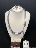 Full view of the lot showing the double strand grey pearl necklace on a white bust with a silvertone clasp, stretch bracelet on top, and several pairs of earrings on display cards.