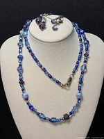 Full view of the necklace displayed on a white bust with both pairs of earrings arranged above it showing matching blue beads and silver details.