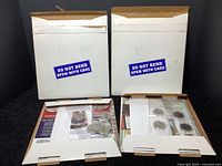 Two white cardboard mailers marked with 'DO NOT BEND OPEN WITH CARE' containing coin sets and ephemera, some mailers unopened at time of cataloguing.