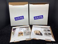 Two unopened white cardboard mailers labeled 'Do Not Bend Open With Care' containing the collection.
