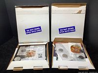 Two mailers opened showing contents including coins, stamps, and paper items inside.