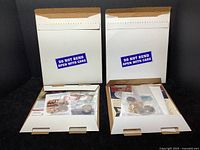 Two white mailers labeled 'Do Not Bend Open With Care' containing coins, stamps, and ephemera.