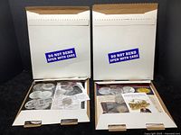 Two white mailers containing the collection, open to show coins, stamps, and ephemera inside.