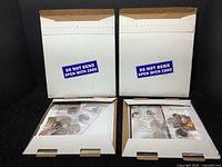 Two white mailers with blue 'Do Not Bend Open With Care' stickers showing outer packaging of the lot items.