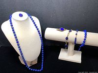 Full view of the jewelry set including necklace on bust, ring, and bracelets on display stand showing blue stones and gold accents.